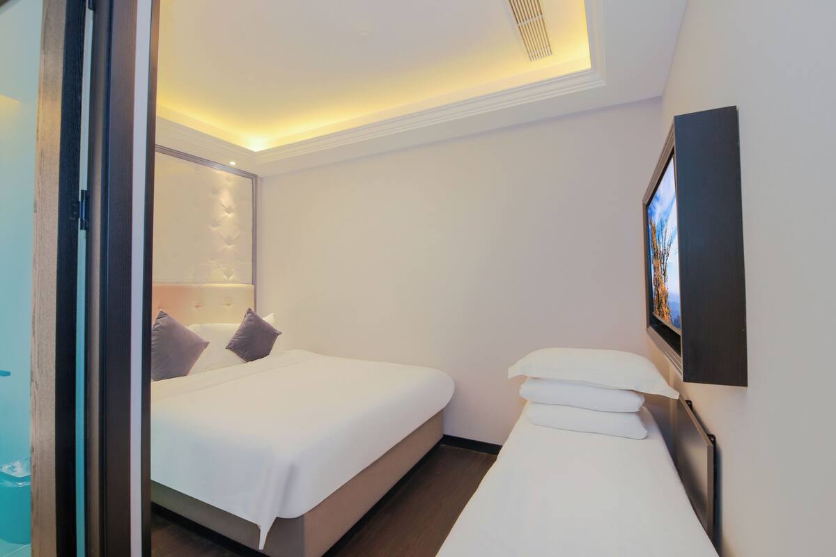 A hotel room with a bed, a bedside table, a wall-mounted TV, and a ceiling light.