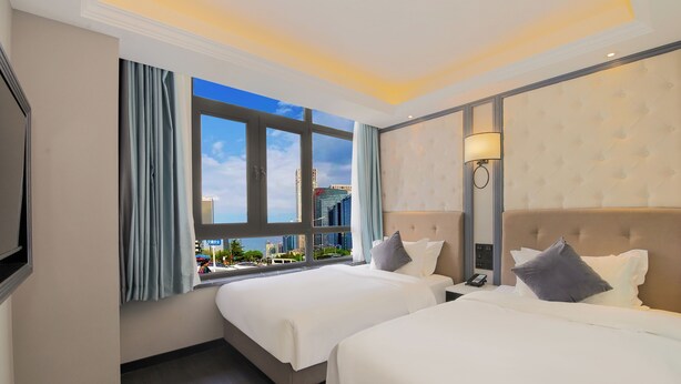 A hotel room with two beds, a large window with curtains, a wall-mounted lamp, and a view of a cityscape. - XiYuan Hotel (Beijing)