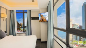 A hotel room with a large bed, a TV mounted on the wall, and a window offering a city view. - XiYuan Hotel (Beijing)
