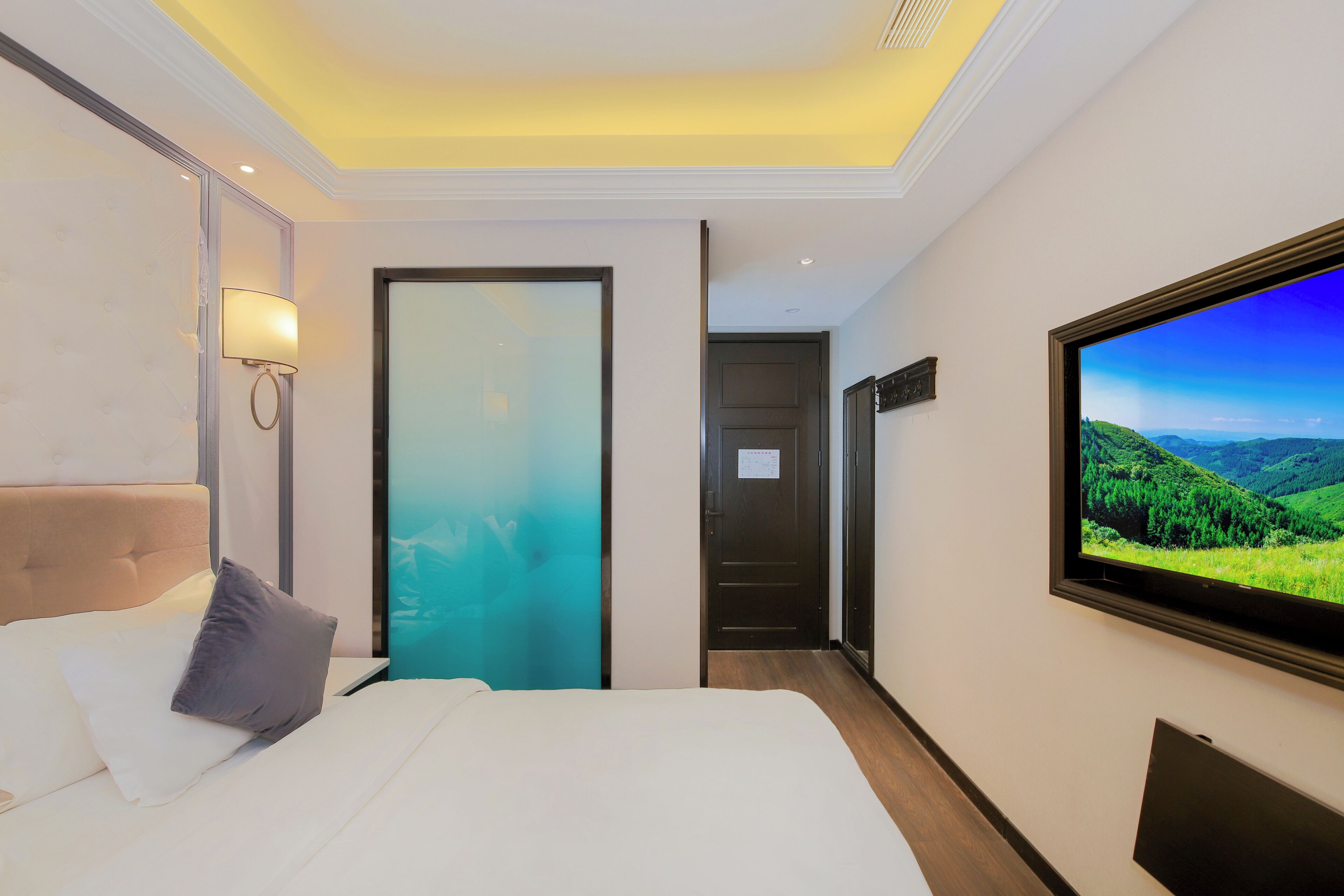 A hotel room with a bed, a TV on the wall, and a door leading to another room.
