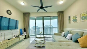 A modern living room with a sofa, a TV, a ceiling fan, and a balcony with a city view. - Teega Residence by Stayrene  (Iskandar Puteri)