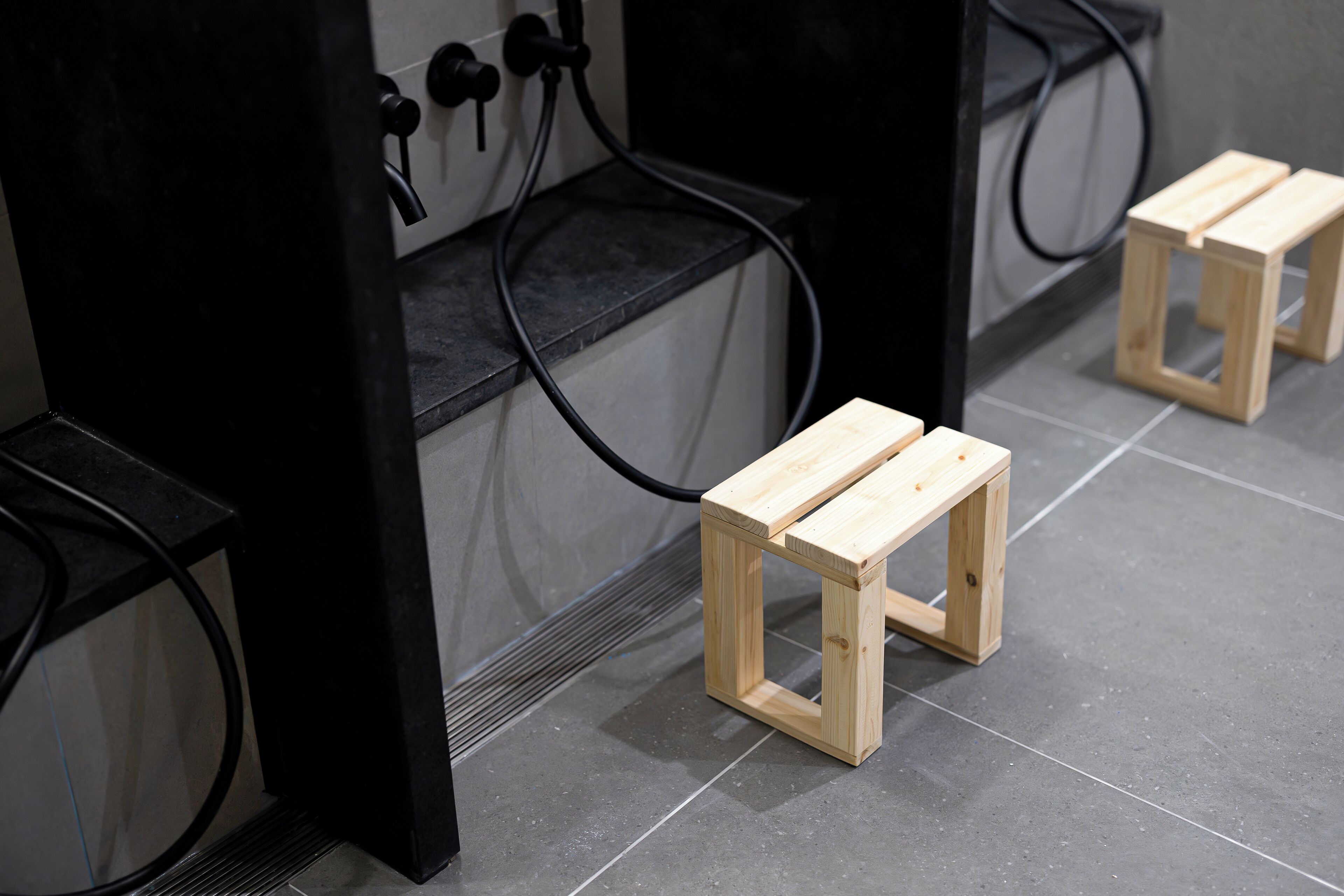 A small wooden stool in a public space with a tiled floor and black metal structures.