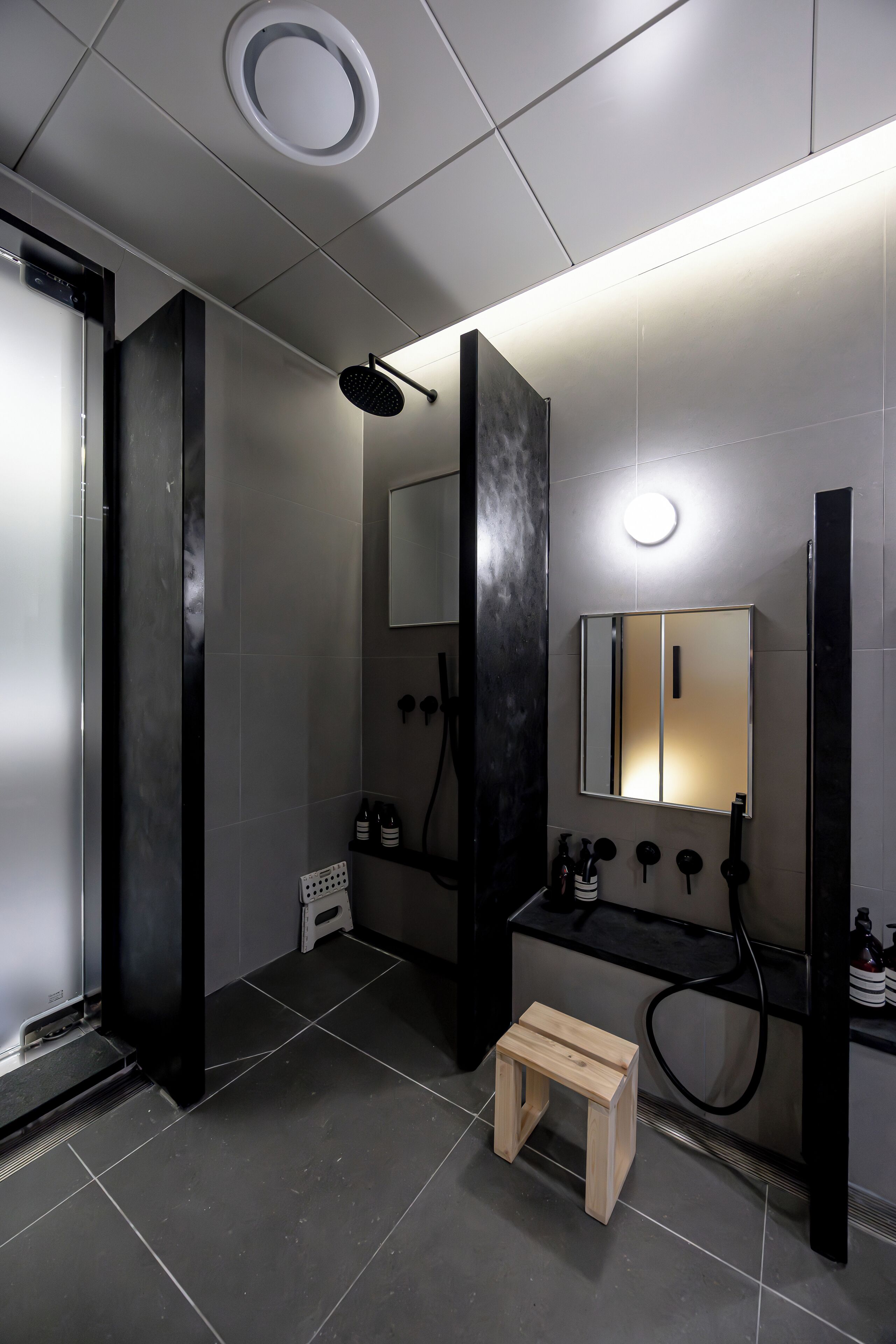 A modern bathroom with a shower, a mirror, and a small wooden stool.