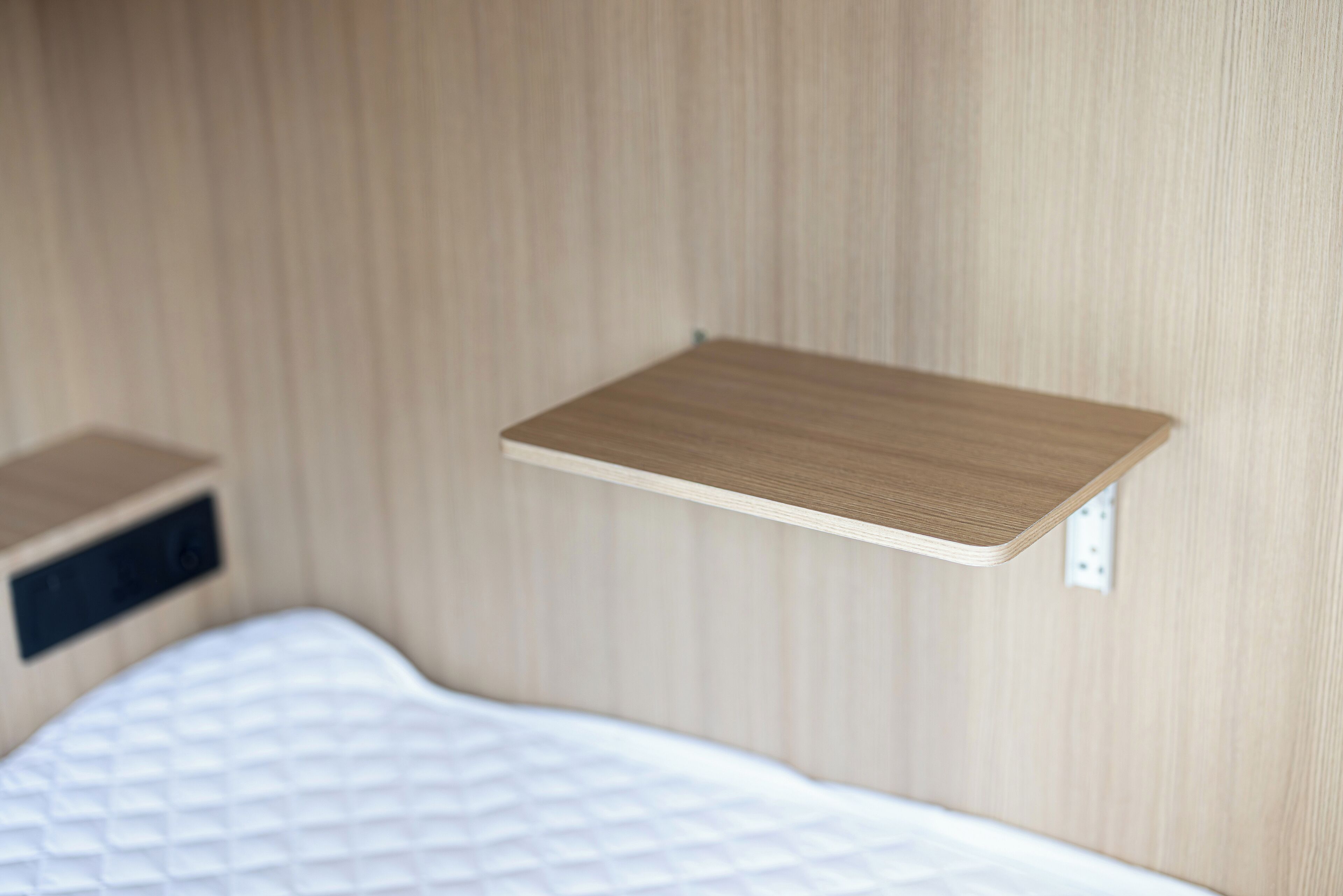 A bed with a quilted mattress and a wooden shelf above it.