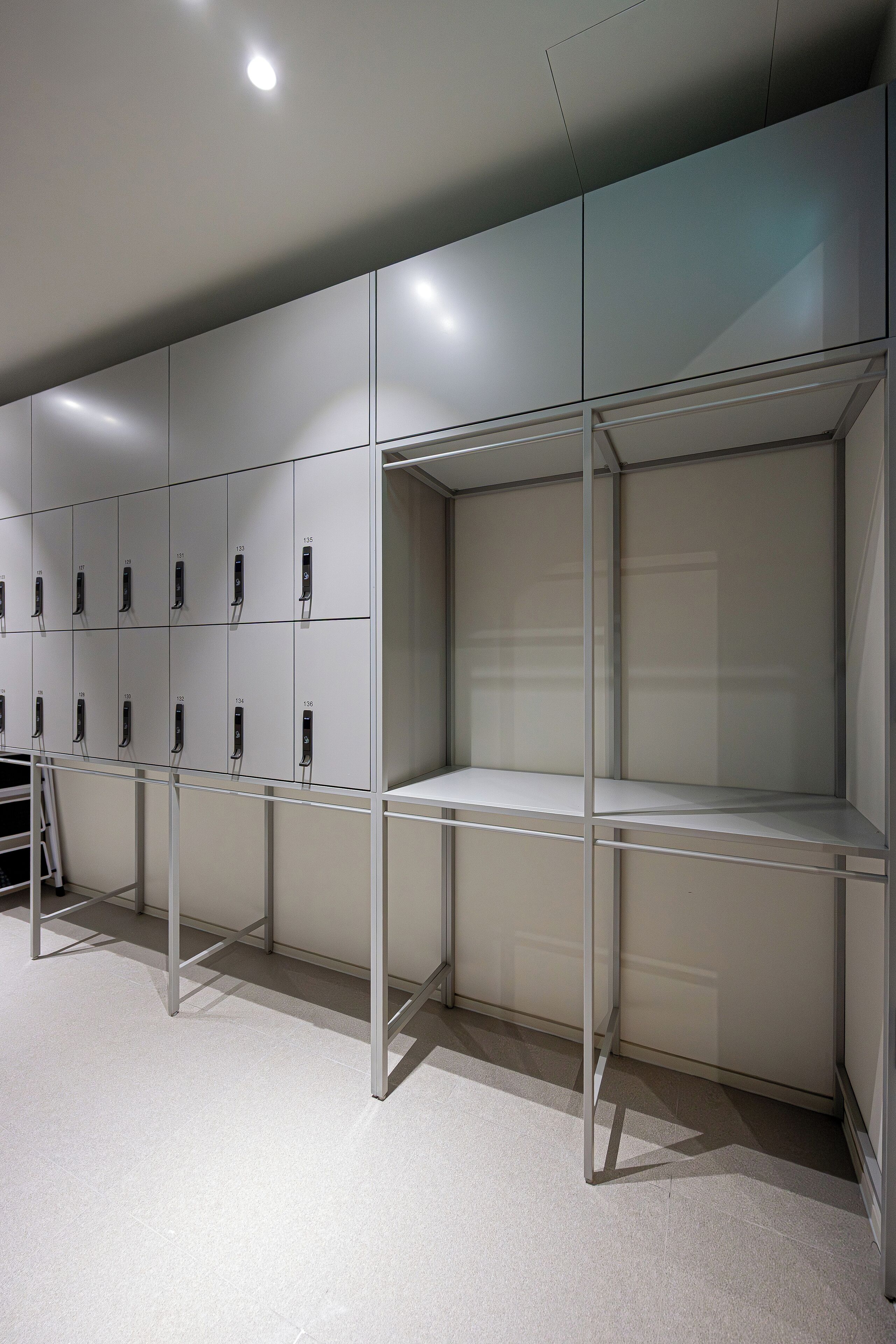 A modern, minimalist locker room with metal lockers and a glass partition.