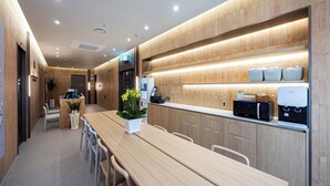 A modern kitchen with wooden cabinetry, a long dining table, and a coffee machine. - Haeundae Marine Capsule Hotel & Spa (Busan)