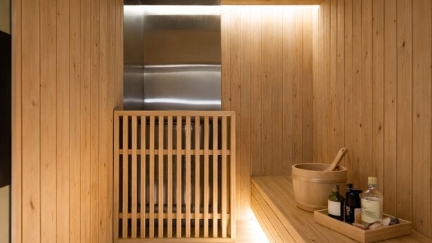 A wooden sauna with a bench, a wooden divider, and a shelf with bottles and a bowl. - Haeundae Marine Capsule Hotel & Spa (Busan)