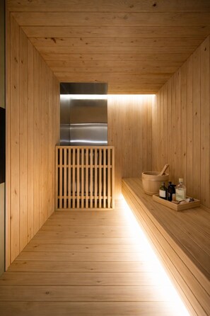A wooden sauna with a bench, a wooden divider, and a shelf with bottles and a bowl. - Haeundae Marine Capsule Hotel & Spa (Busan)