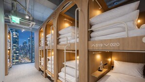 A hotel room with bunk beds, a city view, and a small bedside table with a bottle. - Haeundae Marine Capsule Hotel & Spa (Busan)