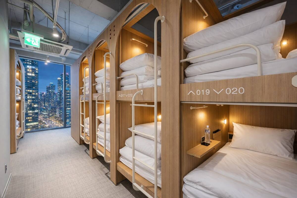 Habitación de hotel con literas, vistas a la ciudad y una mesita de noche con una botella.