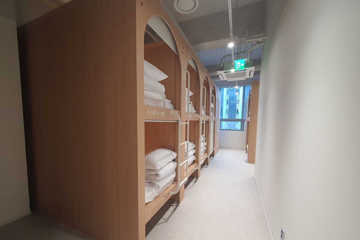 A hotel corridor with bunk beds, a visible exit sign, and a window with a view.