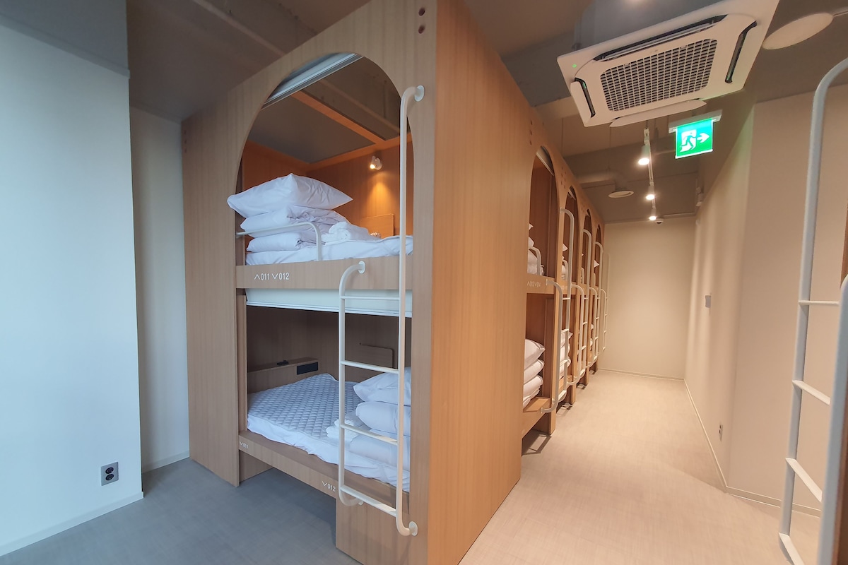 Een hotelkamer met stapelbedden, een kledingkast, en een gang met een groen vluchtlicht.