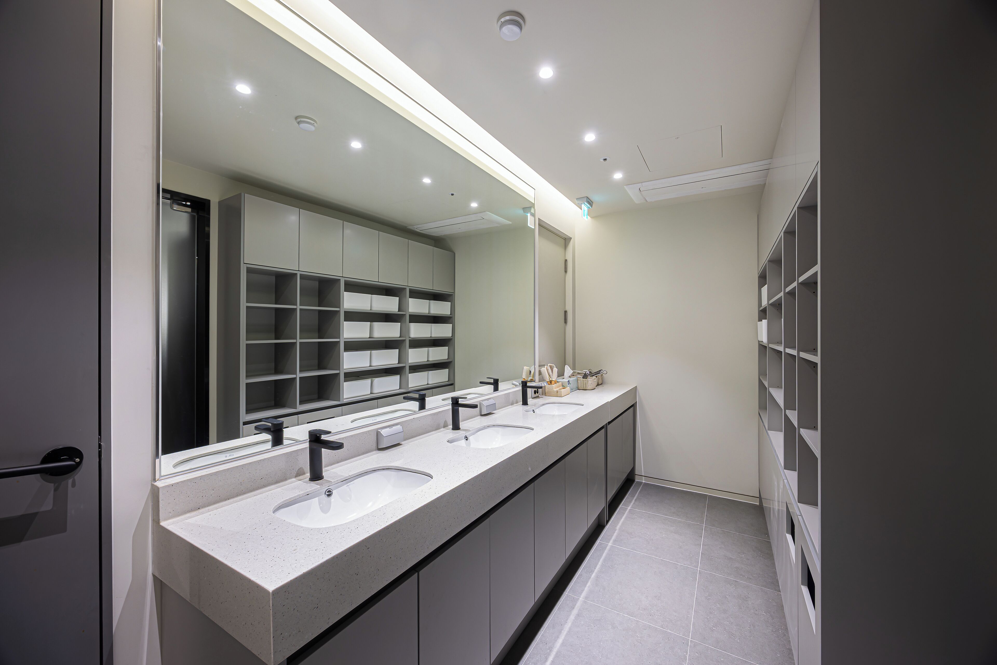A modern bathroom with three sinks, a large mirror, and built-in shelving.