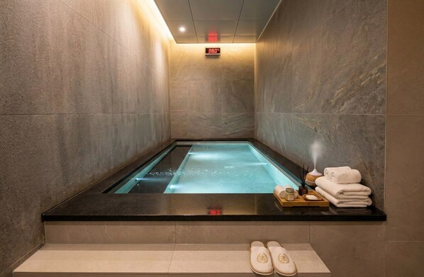 A spa room with a hot tub, a digital thermometer, towels, and slippers on the floor. - Haeundae Marine Capsule Hotel & Spa (Busan)