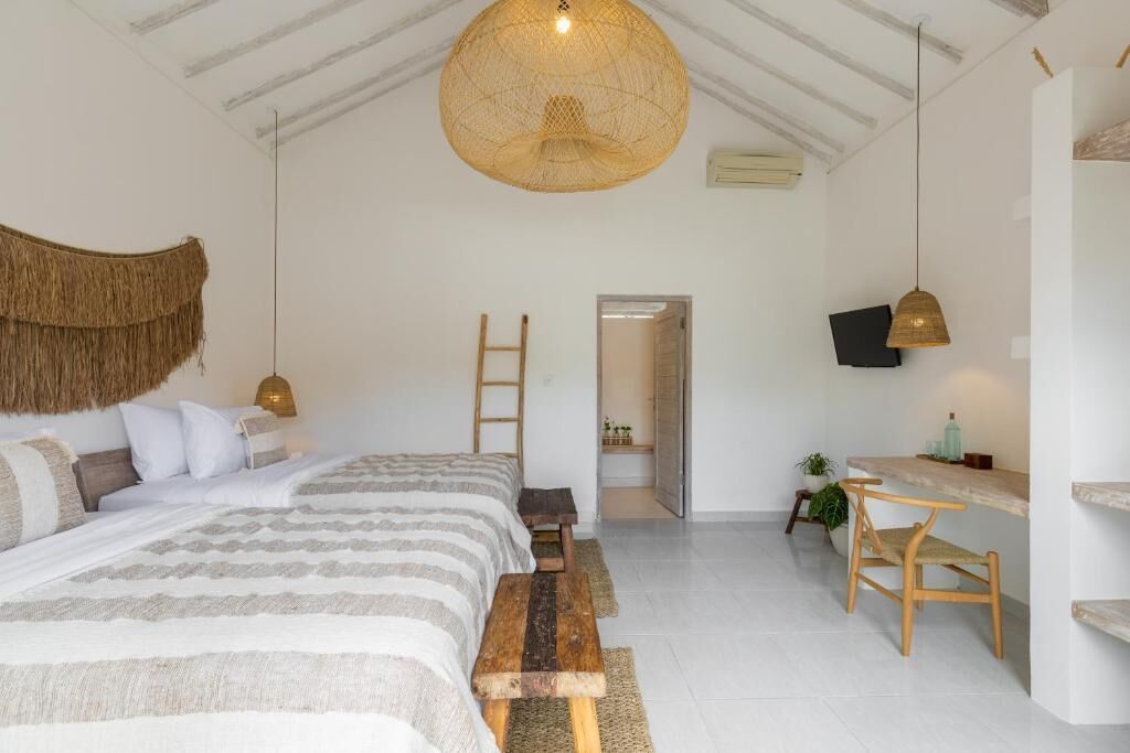 A bedroom with a bed, a desk, and a chair. There is a ladder leaning against the wall and a hanging light fixture.
