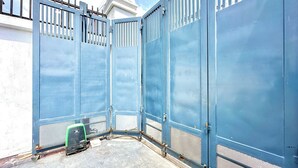 Ein blaues Metallgatter mit einem Drahtgeflecht, ein kleines grünes Objekt am Boden und ein weißes Gebäude im Hintergrund.
