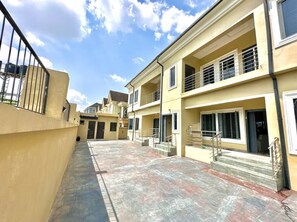 A residential building with multiple balconies, a paved courtyard, and a clear sky. - 2-bedroom Apartment in serene Opic Estate with AC comfort (Opic)