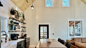 A modern kitchen with wooden cabinets, a central island, and built-in shelves with plants and kitchenware.
