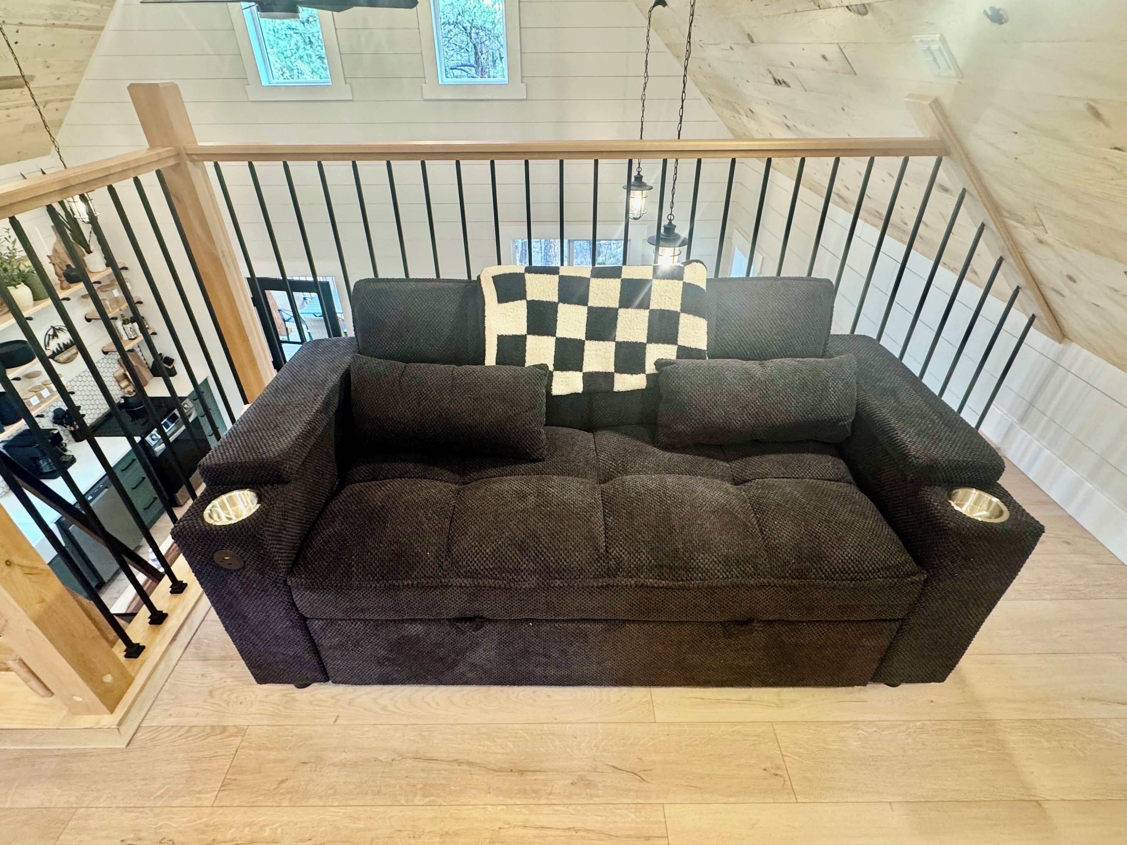 A dark brown sofa with a checkered throw pillow in a room with wooden walls and a glass railing.