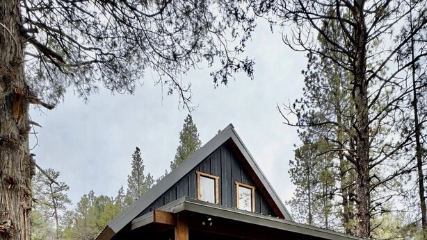 A cabin with a wooden deck, large windows, and a stone foundation.