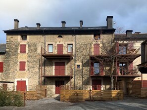 A multi-story stone building with red shutters, balconies, and a gated entrance.