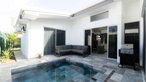 Ett modernt utomhusområde med en pool, en grå hörnsoffa och en grill.