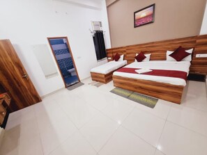 A hotel room with a wooden bed, a small desk, a chair, a window with curtains, and a wall-mounted air conditioner. - Shree Krishana Dham  (Vrindavan)