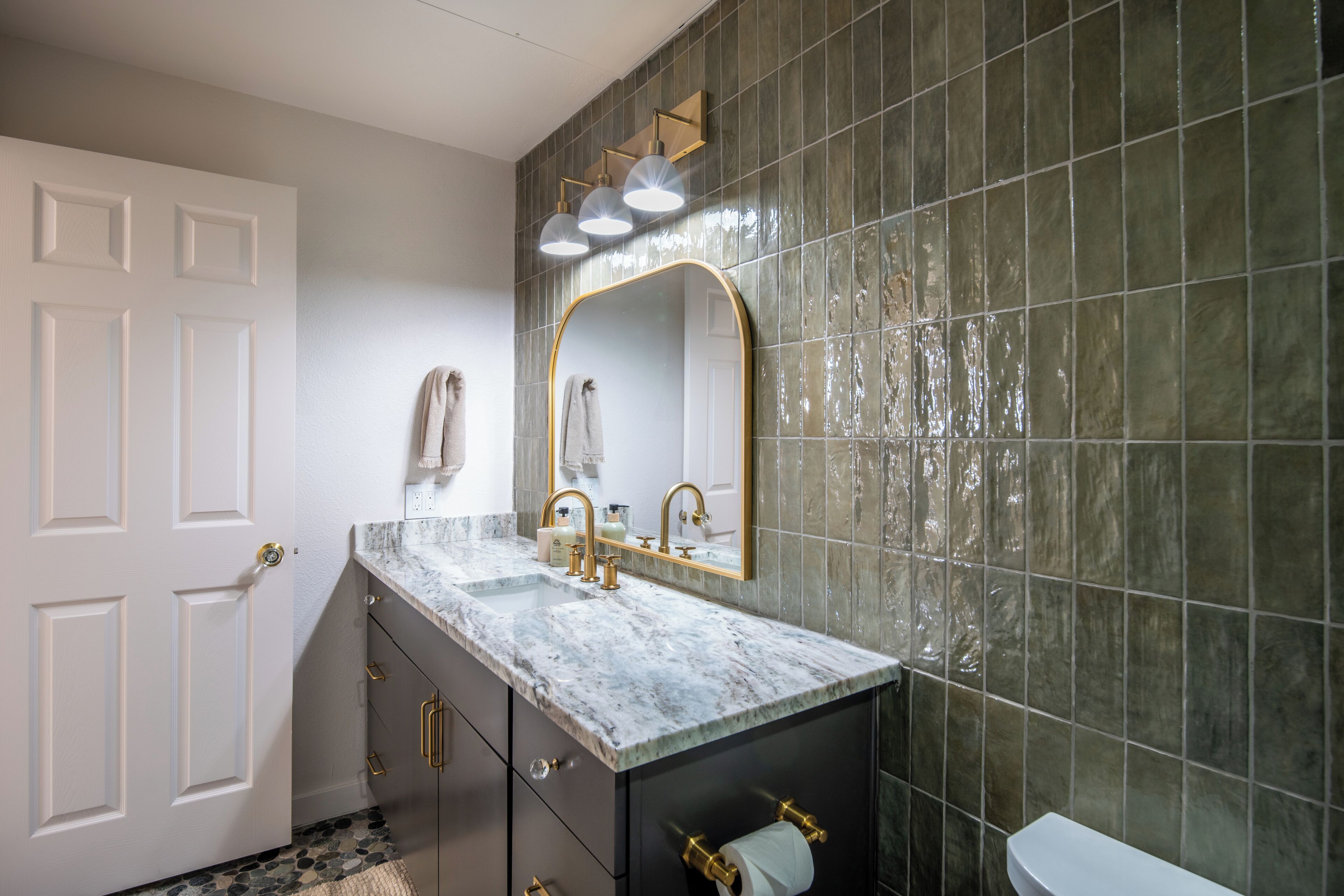 A bathroom with a marble countertop, a gold-framed mirror, and a toilet.