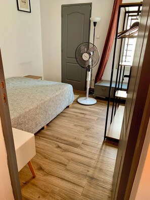 A bedroom with a bed, a standing fan, a door, and a window.