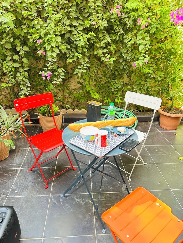 A patio with a table set for two, surrounded by potted plants and a red chair.