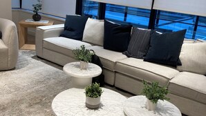 A modern living room with a beige sofa, three round marble coffee tables with potted plants, and a view of a pool through large windows. - Top of Mission living (Mission)