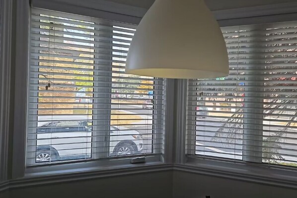 A room with a large window featuring horizontal blinds, a white ceiling lamp, and a view of parked cars outside.