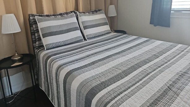 Ein ordentlich bezogenes Bett mit gestreifter Bettwäsche, zwei Nachttischlampen und ein Fenster mit Vorhängen.