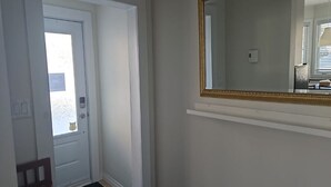 Ein Korridor mit einer weißen Tür, einem Holzstuhl und einem Spiegel an der Wand.