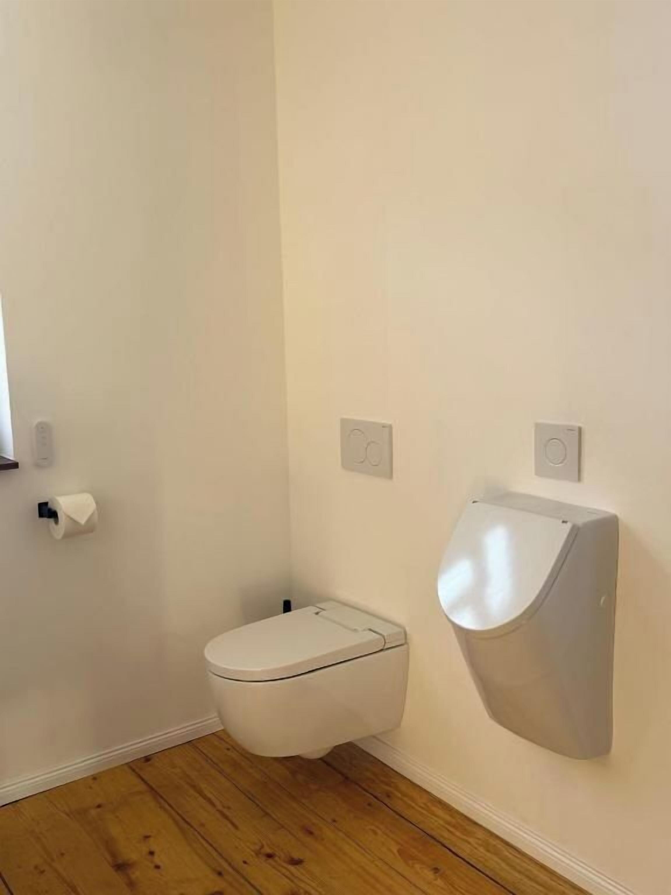Ein Badezimmer mit einer weißen Toilette, einem wandmontierten Bidet und einem Toilettenpapierhalter.