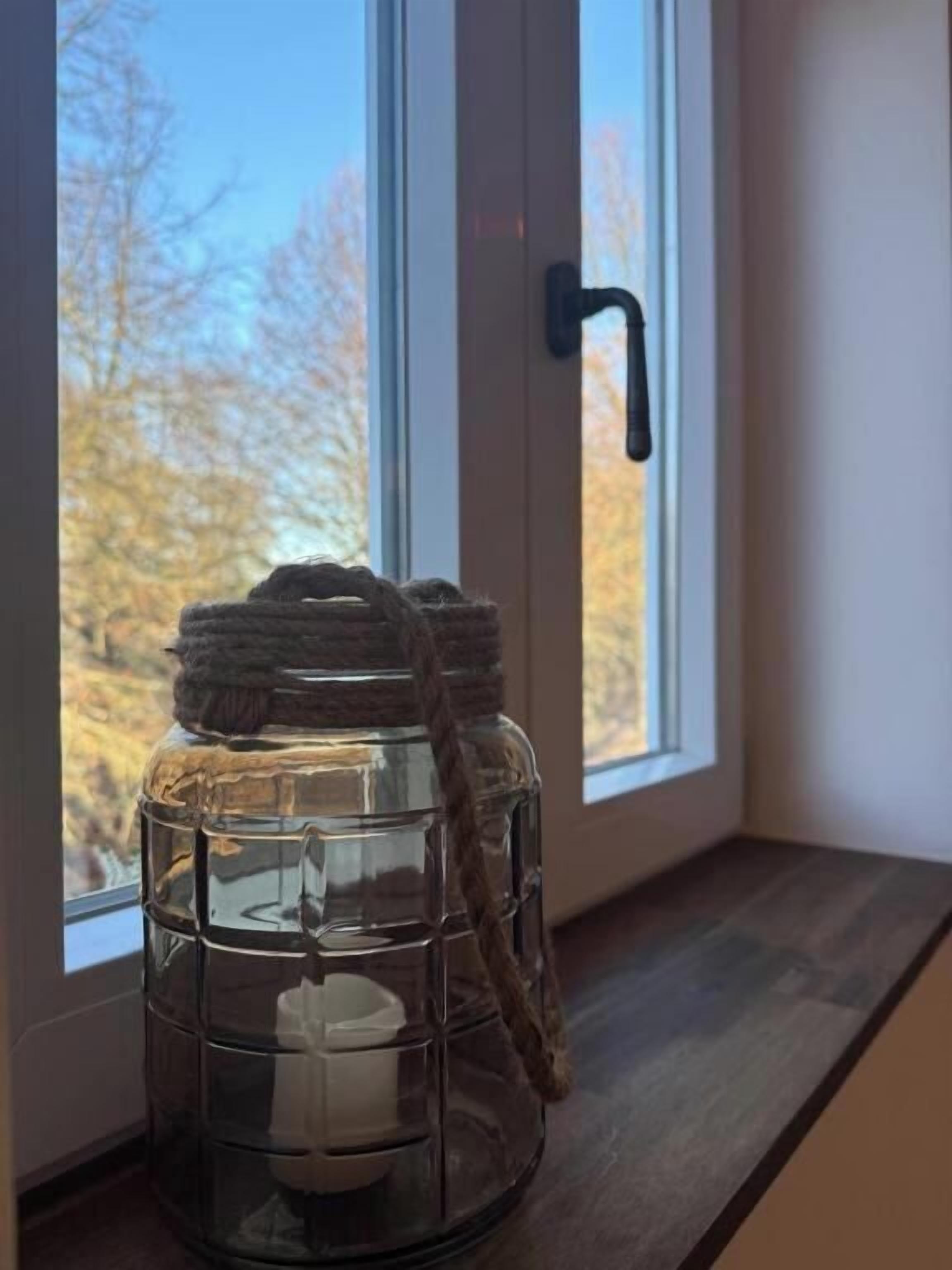 A clear glass lantern with a candle inside, placed on a window sill.