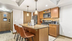 A modern kitchen with a central island, bar stools, wooden cabinets, stainless steel appliances, and pendant lighting. - Contemporary 2BR w/ hot tub and Mountain Views (Dead Man`s Flats)