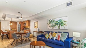 A modern living room with a blue sofa, a dining area with a wooden table, and a kitchen with wooden cabinets. - Contemporary 2BR w/ hot tub and Mountain Views (Dead Man`s Flats)