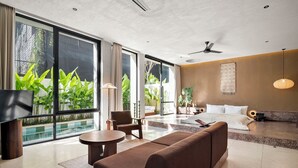 A modern hotel room with a large bed, a sofa, a TV, and a balcony with plants. - The Craft Hotel Ubud (Ubud)