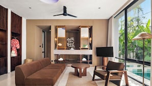 A modern living room with a sofa, a round table, a TV, and a view of a swimming pool. - The Craft Hotel Ubud (Ubud)