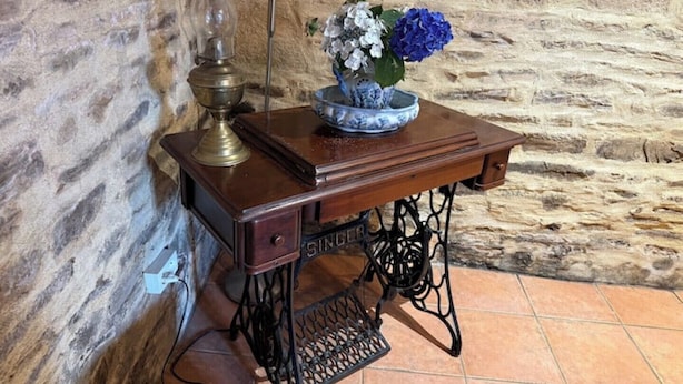 Eine alte Nähmaschine mit Holztisch, einer Messinglampe und einer Blumenvase.