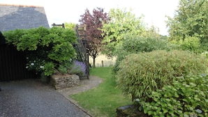Ein Garten mit Kiesweg, Steinmauern und verschiedenen Sträuchern und Bäumen.