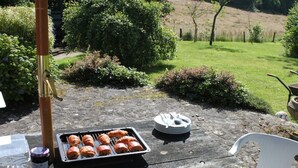 Ein Tisch mit einer Tablett voller Croissants und einer Geschirrplatte, auf einer Steinterrasse mit Blick auf einen Garten.