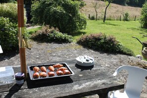 A table with a tray of croissants and a plate with utensils, set on a stone patio with a garden view.