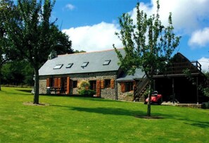 A stone building with a sloped roof and multiple skylights, surrounded by a well-maintained lawn and trees.