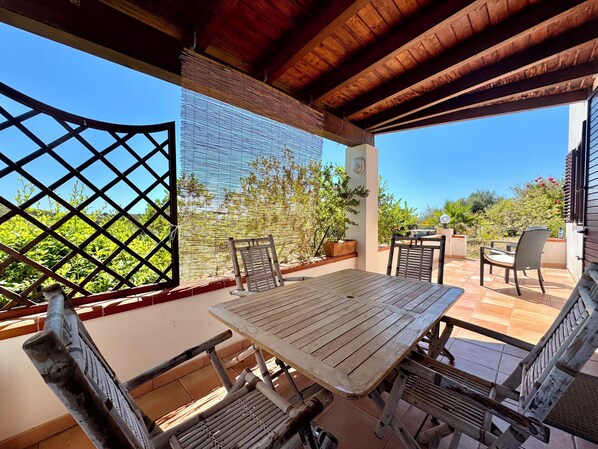 A covered patio with a table and chairs, a wooden ceiling, and a view of greenery. - " Blue Design Apartment " (Tortolì)