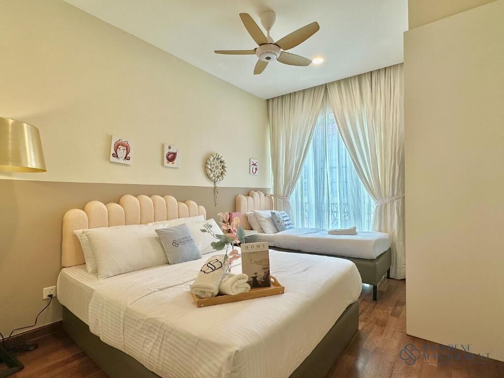 A bedroom with a bed, a ceiling fan, a window with curtains, and a bedside table with a book and towels.