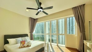 Ein Schlafzimmer mit Bett, Deckenventilator, einem Fenster mit Vorhängen und Blick auf hohe Gebäude.
