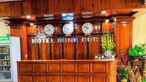 A wooden reception desk with clocks, a sign reading 'HOTEL MINH DUC,' and a decorative plant. - Minh Duc 2 Hotel (Trung Khanh)