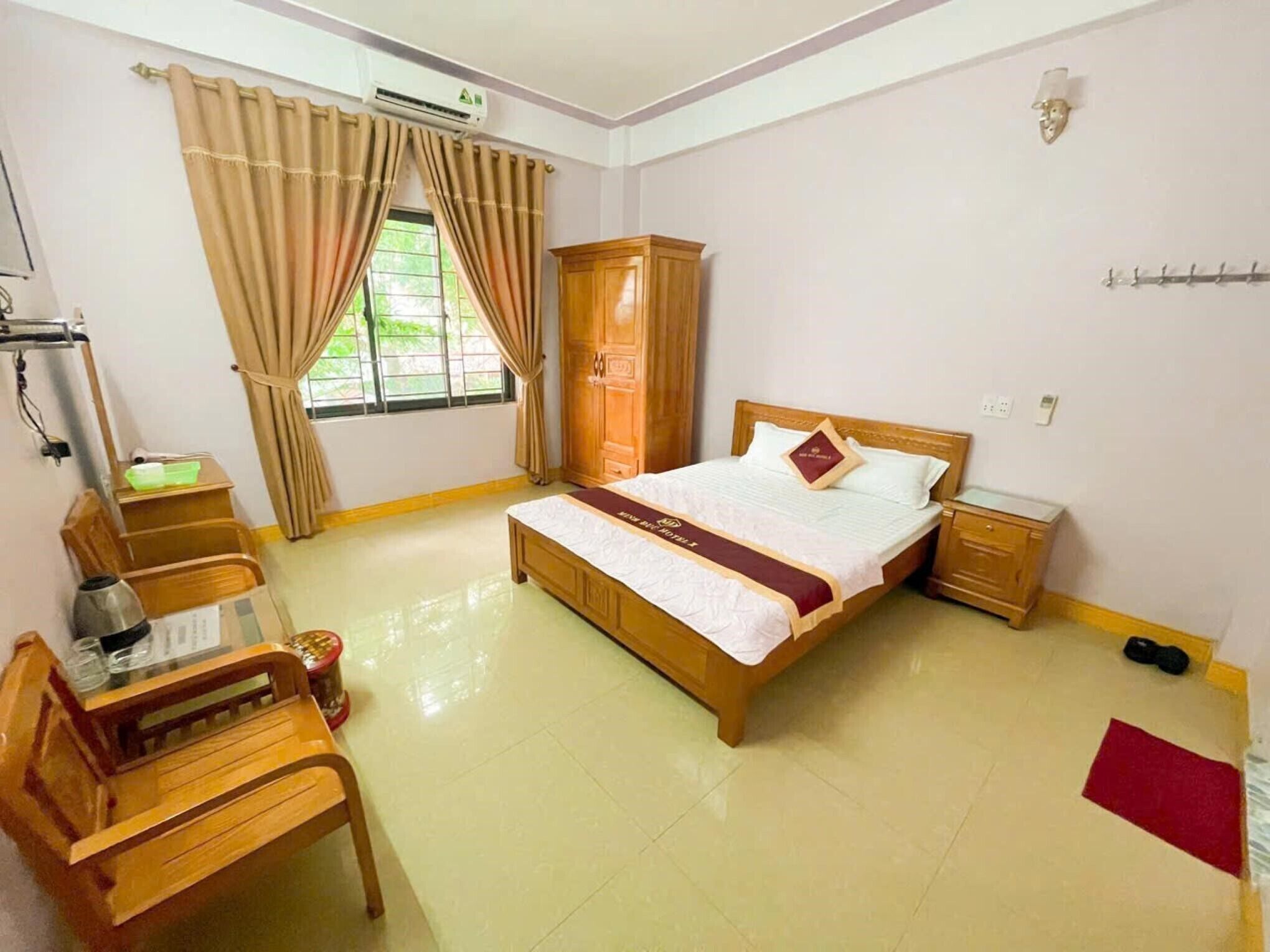 Habitación de hotel con cama, muebles de madera, escritorio, silla, armario y ventana con cortinas.